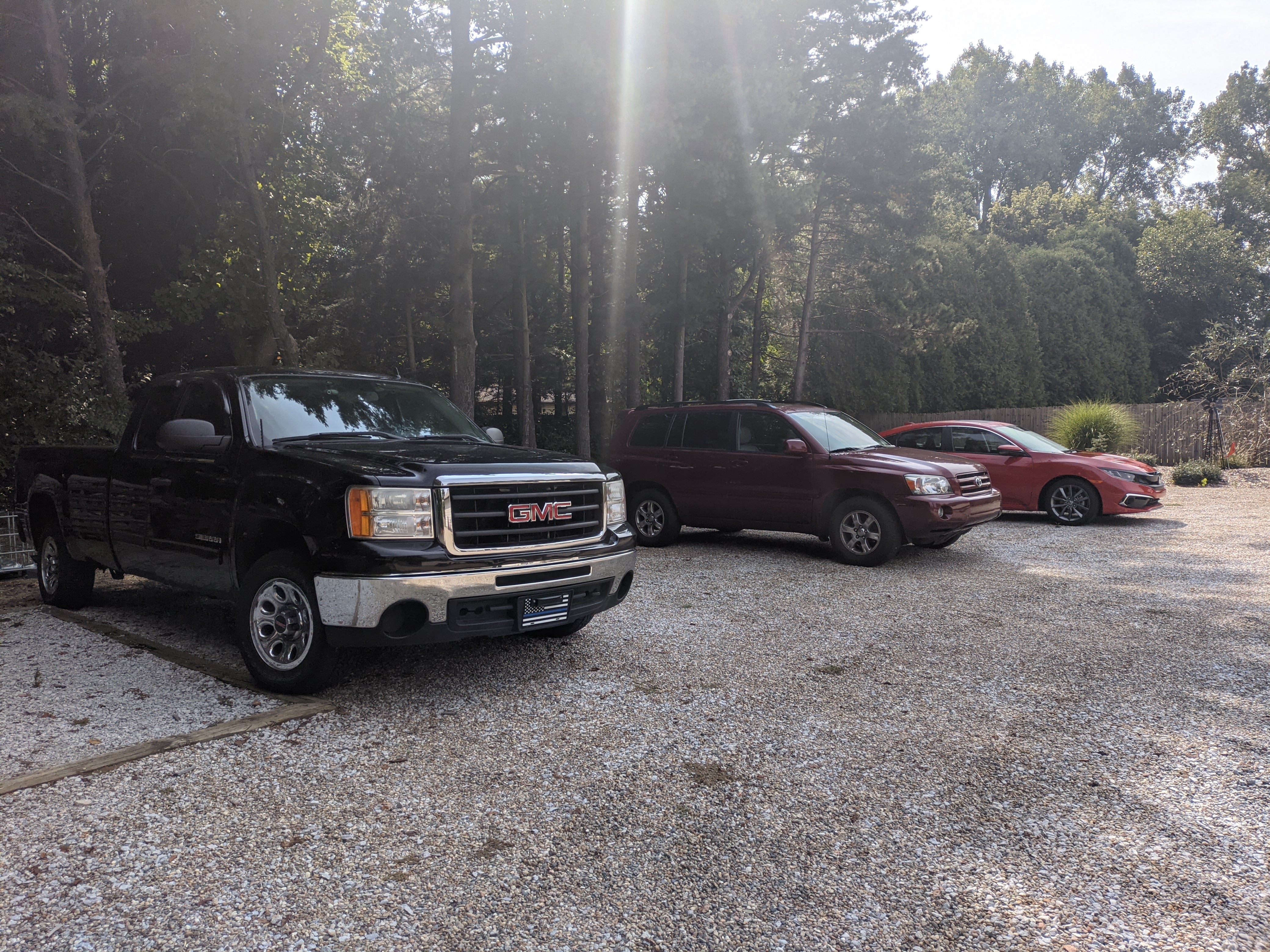 Sunbeaming down onto three cars parked next to each other with woods behind them